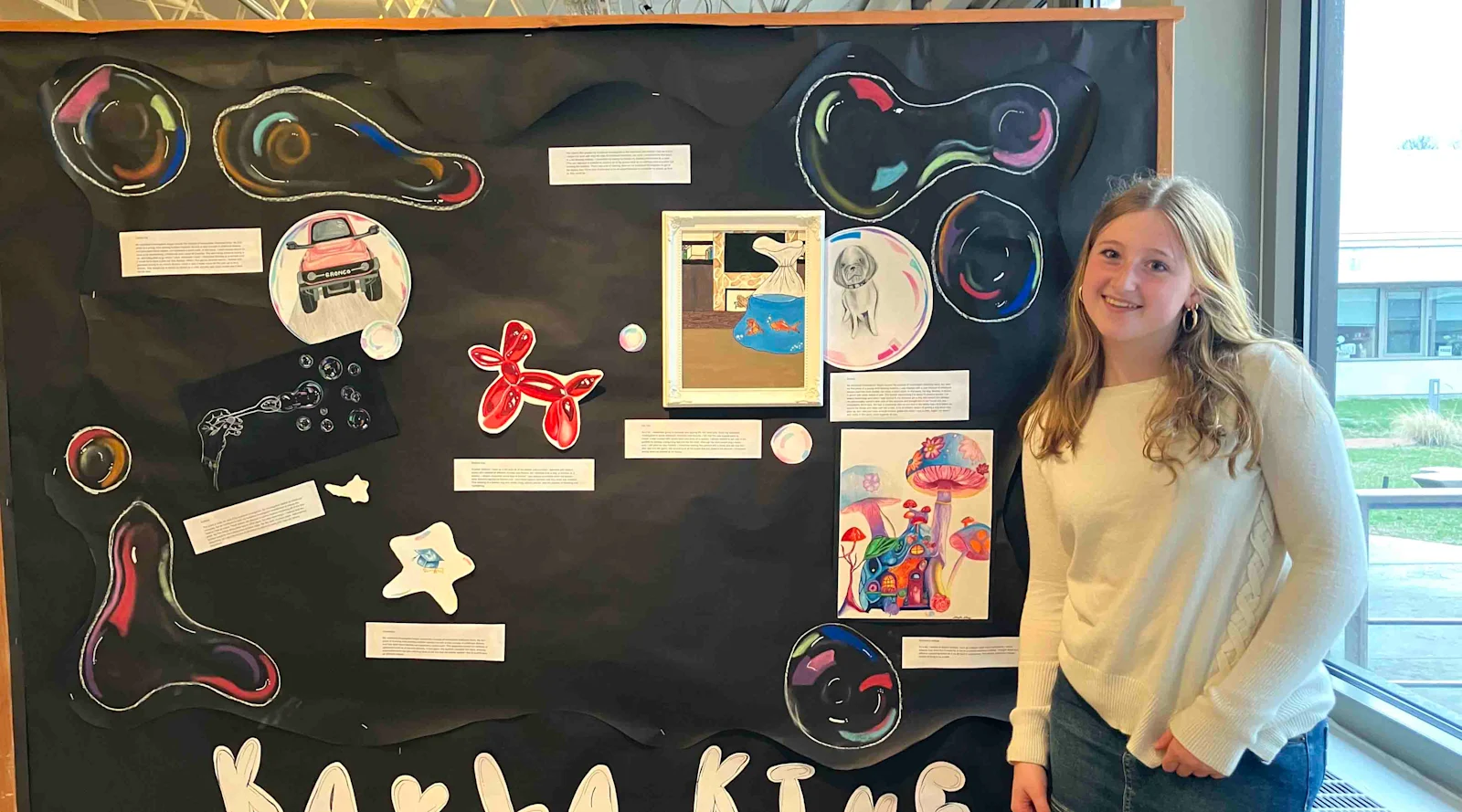 students smiles in front of her work at the AP Art Exhibit